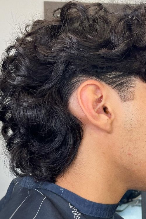 Dark curly subtle mullet with undercut fade.