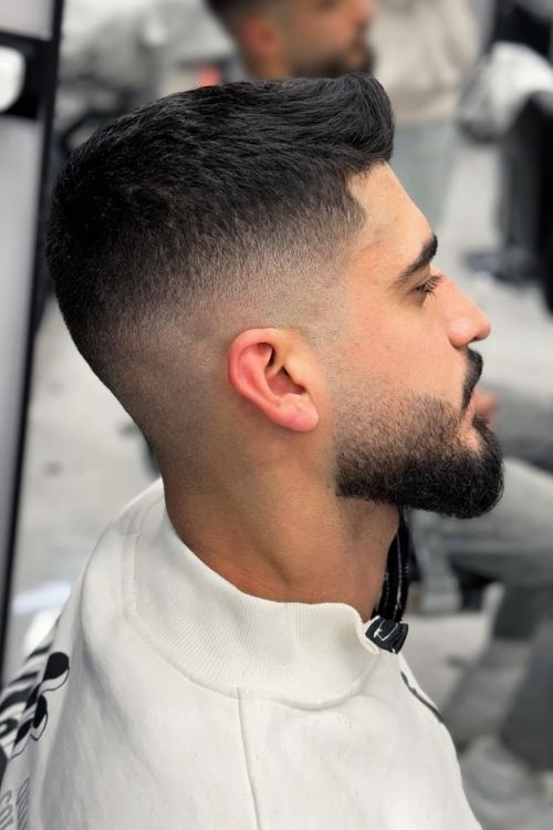 Faded crew cut with natural black hair featuring a low skin fade and well-groomed beard