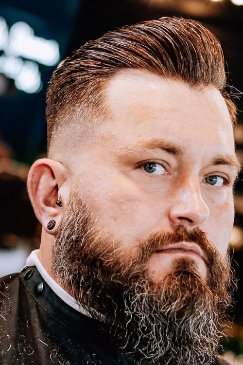 Slicked-back fade with medium brown hair featuring a high fade and full thick beard